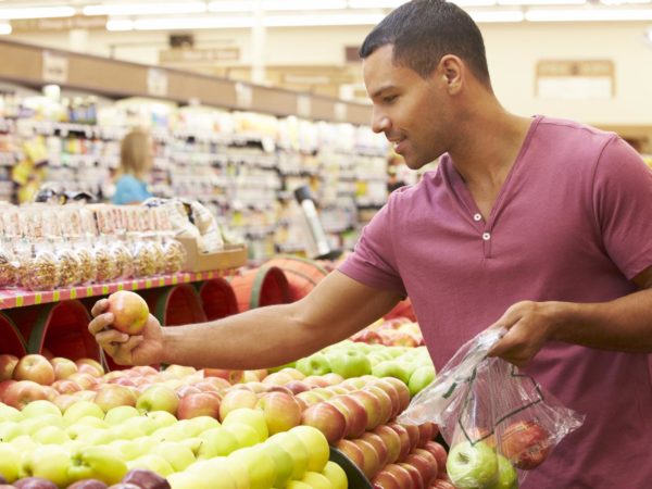 Man At Fruit Counter In Supermarket Putting Fruit Into A Bag