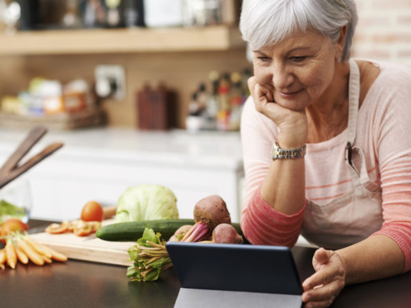 Shot of a woman resting her chin on her hands as she watches a tablet in her kitchen