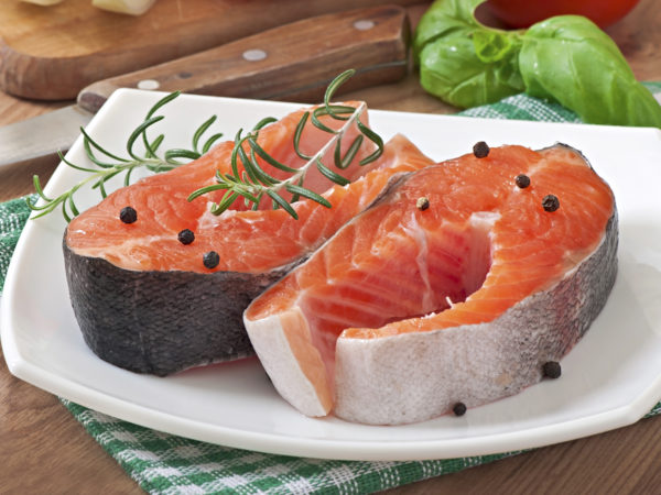 Fresh and raw steaks trout on a wooden cutting board with sliced lemon, rosemary and pepper