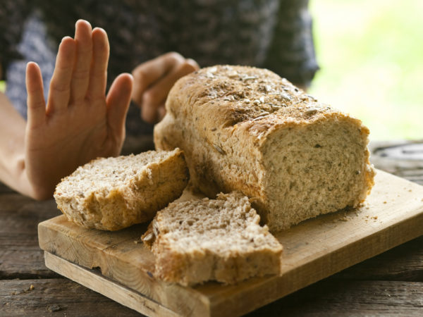 A woman rejecting bread, gluten-free concept. A whole-grain loaf of bread on a rustic wooden table, and a woman rejecting it with a hand gesture.