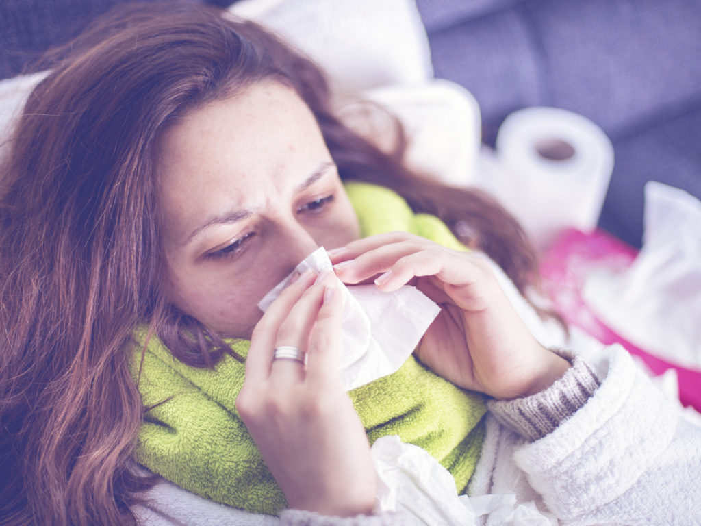 Close up of a young woman sneezing into a tissue.