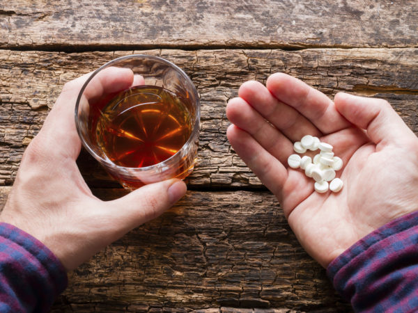 man holding a glass of alcohol and a handful of pills