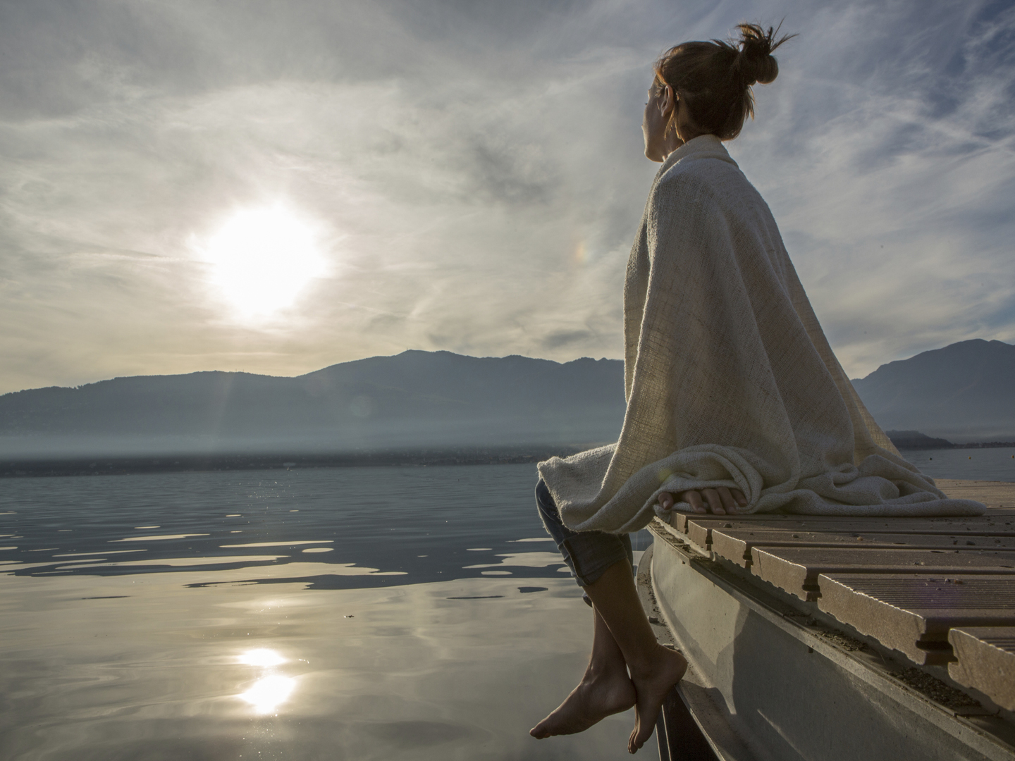 Young woman relaxes on lake pier, watches sunset. Beautiful Autumn day in Italy.