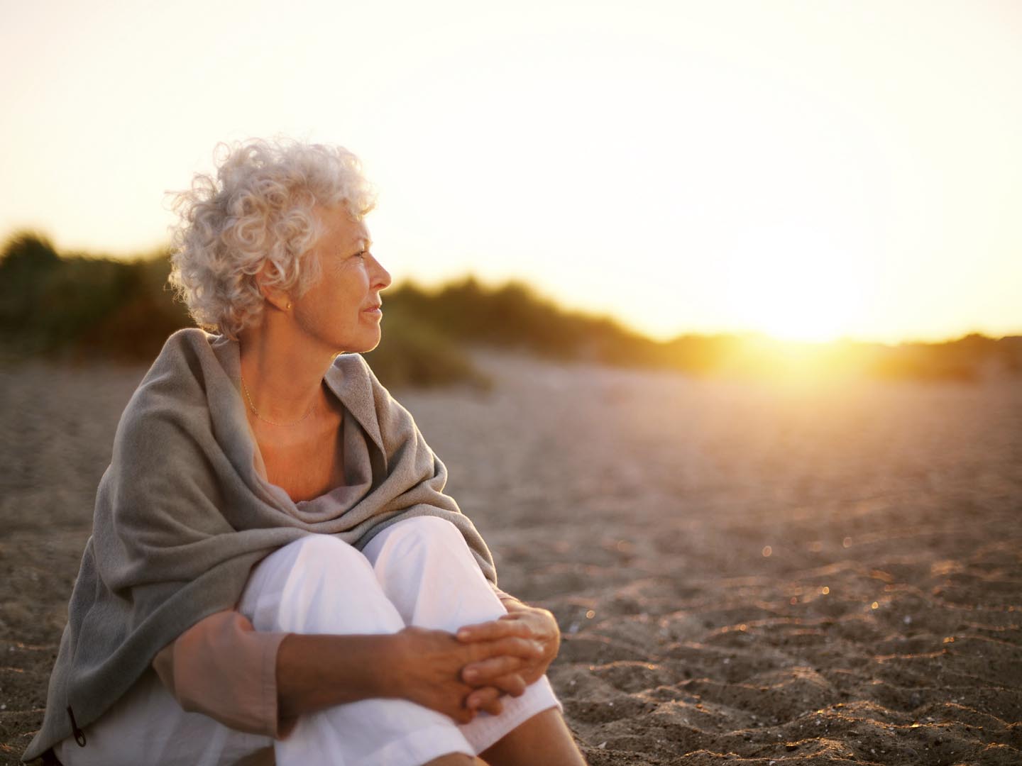 Old woman sitting on the beach looking away at copyspace. Senior female sitting outdoors