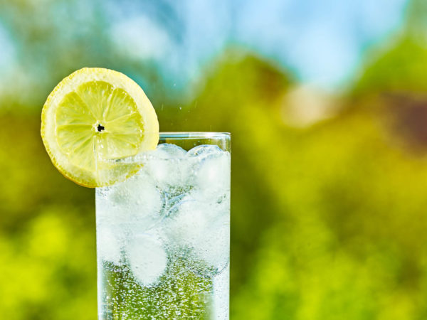 Sparkling water and lemon slice on glass with an ice, sunny day - narrow focus on middle of the glass