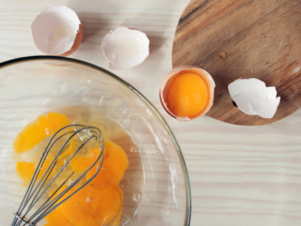 Cracked eggs in a bowl with a whisk atop wooden kitchen counter.