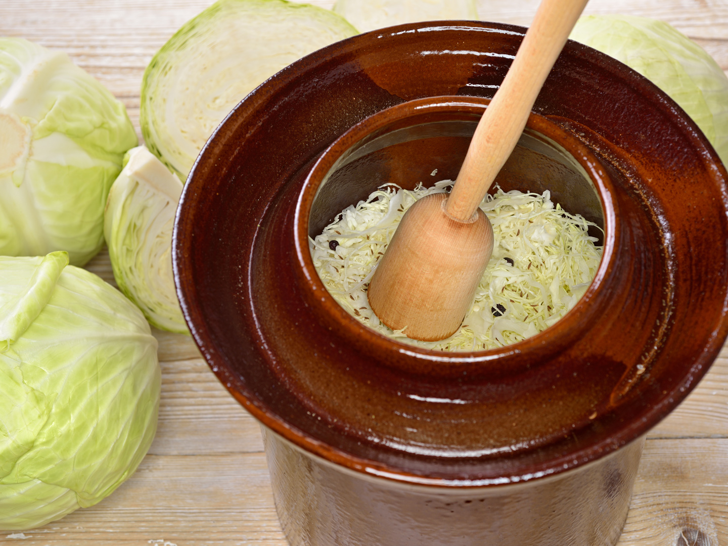 Food fermentation, making sauerkraut: White cabbage with a wooden pounder in a ceramic harvest crock