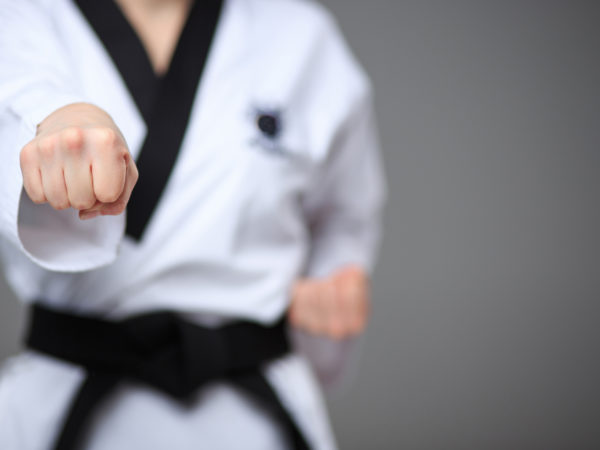 The hand of karate girl in white kimono and black belt training karate over gray background.