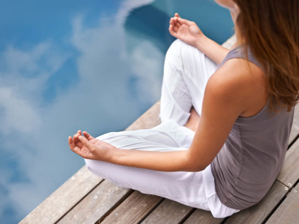 Cropped closeup of a young woman meditating poolside