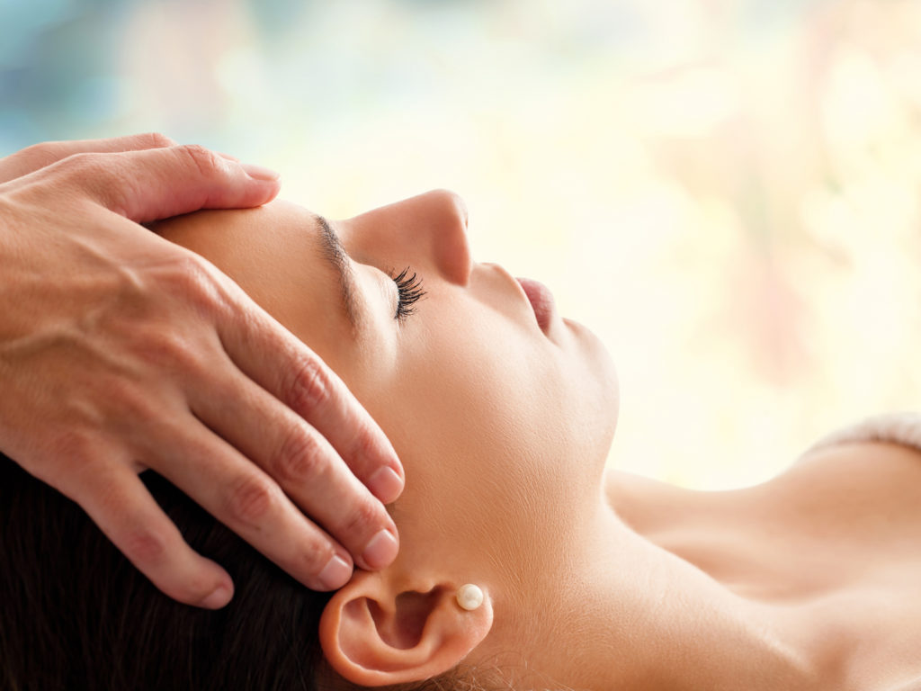Close up head portrait of young woman having facial massage in spa. Therapist massaging womans head against colorful background.