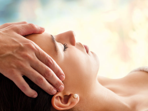 Close up head portrait of young woman having facial massage in spa. Therapist massaging womans head against colorful background.