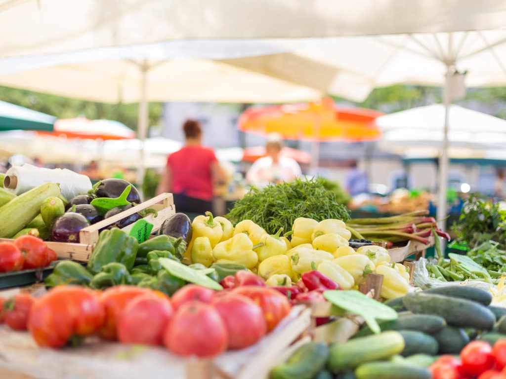 Farmers' food market stall with variety of organic vegetable. Vendor serving and chating with customers.