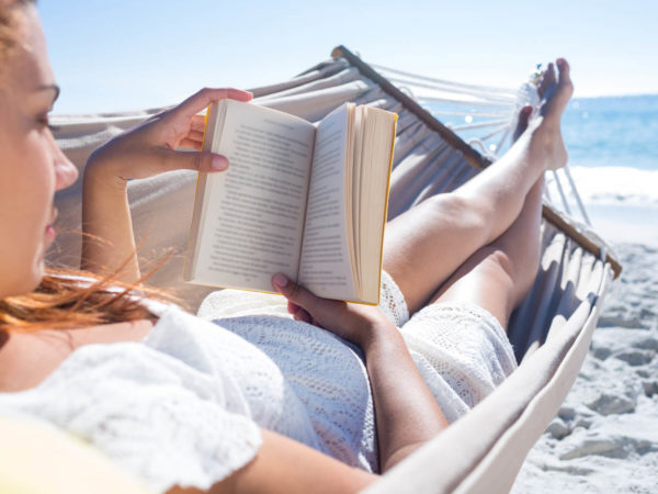 Brunette reading a book while relaxing in the hammock at the beach