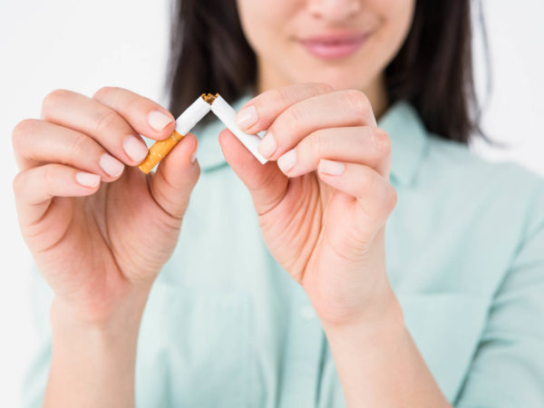 Smiling woman snapping cigarette in half on white background