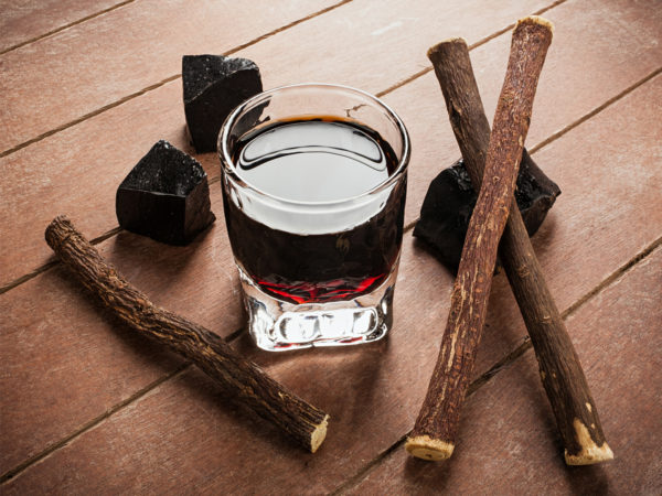 Licorice liqueur with pure blocks and roots on wooden table.