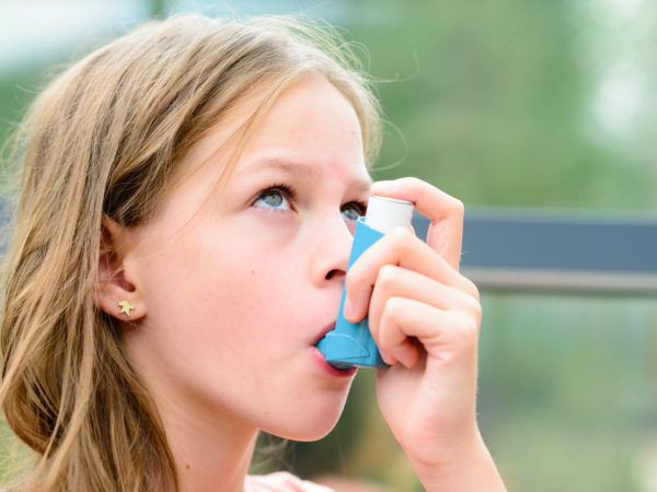 Girl having asthma using the asthma inhaler for being healthy - shallow depth of field - asthma allergy concept