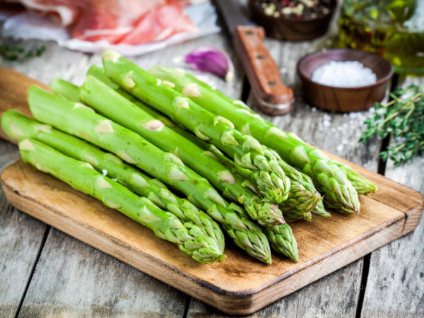 Fresh organic asparagus on a cutting board with Parma ham on a rustic table