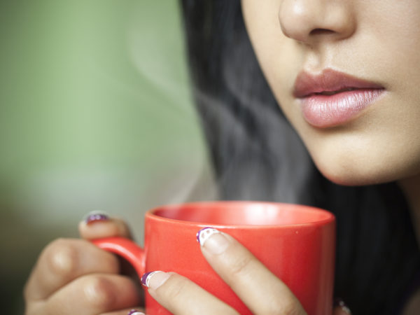 Indoor cropped close-up image of a beautiful Asian young woman holding a hot steaming coffee mug. One person, horizontal composition with selective focus and copy space.