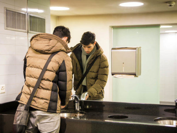 Reflection of young man washing hands in public bathroom