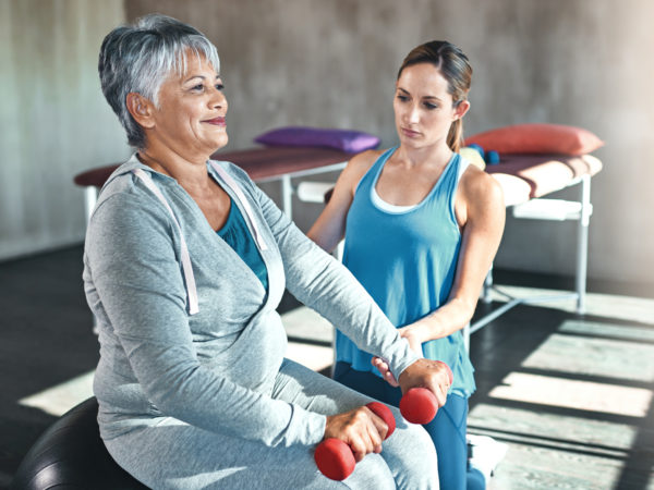 Shot of a senior woman using weights and a fitness ball with the help of a physical therapist