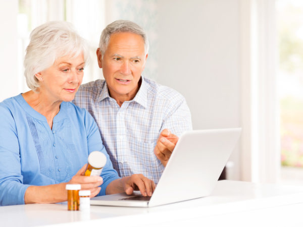 Senior couple with pill bottles browsing internet on laptop at home. Horizontal shot.