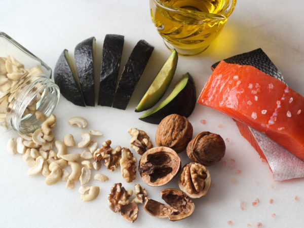 Salmon, olive oil, avocado, walnuts, cashews, rock salt overhead shot on white marble background