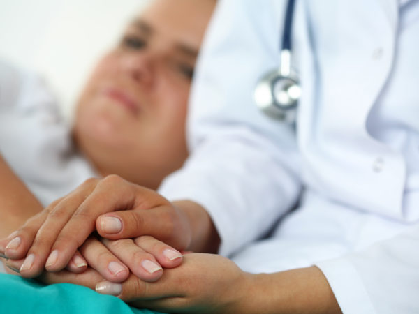 Friendly female doctor hands holding patient hand lying in bed for encouragement, empathy, cheering and support while medical examination. Bad news lessening, compassion, trust and ethics concept