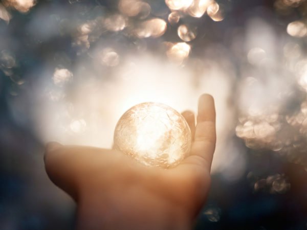 unrecognizable witch hand holding magic globe, defocused lights in background.