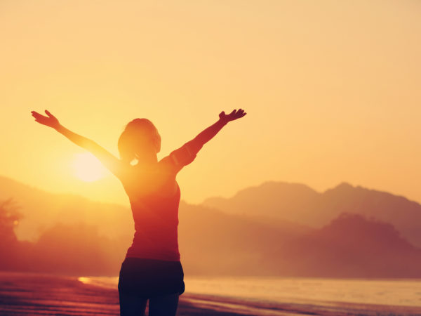 cheering woman open arms to sunrise at seaside