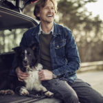 Photo of a man sitting in the car and cuddle his dog