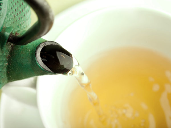 Green tea being poured out of a Japanese teapot, selective focus.