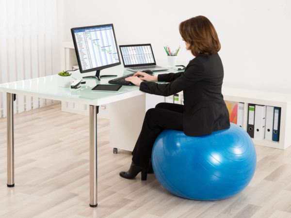 Young Businesswoman Sitting On Pilates Ball Working In Office