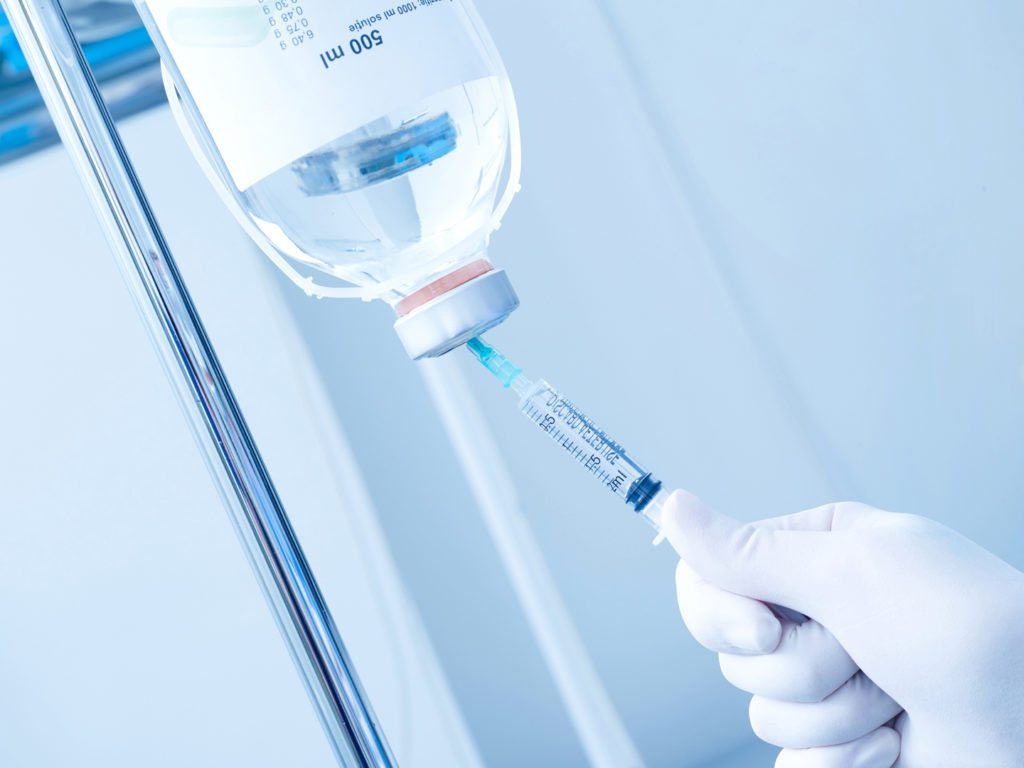 Hand with protective glove, syringe and infusion