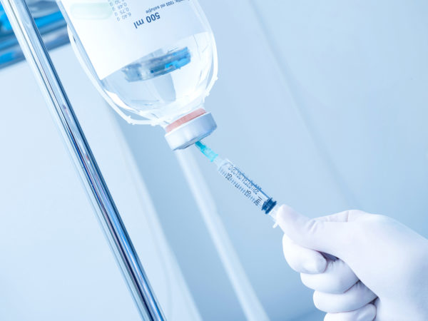 Hand with protective glove, syringe and infusion