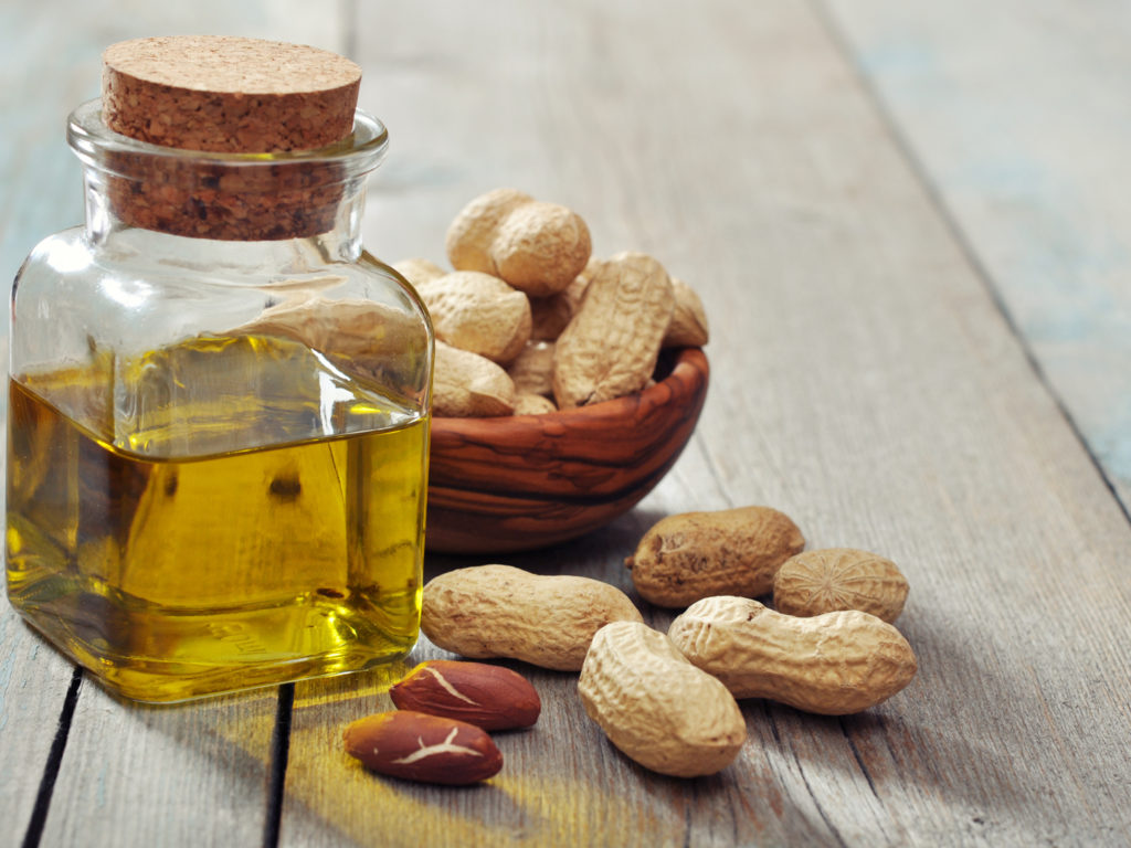 Peanut oil with raw peanuts on wooden background