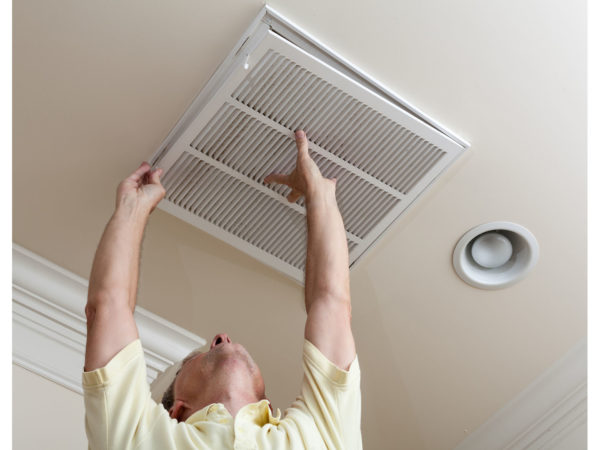 Senior male reaching up to open filter holder for air conditioning filter in ceiling