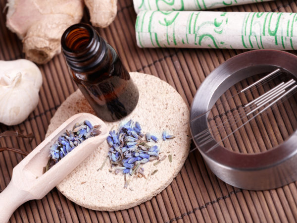 Acupuncture needles laying on the stone mat, moxa sticks on wooden desk and lavender petals with macerated oil. TCM Traditional Chinese Medicine concept photo