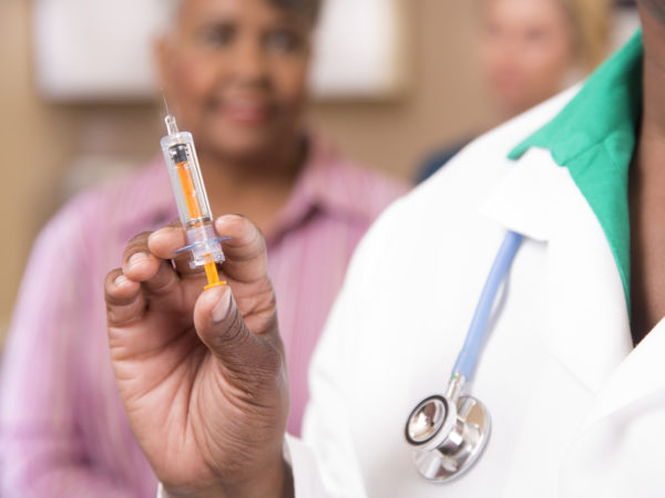 Close up view of doctor or nurse preparing a flu vaccine for African descent, senior adult patient at a local medical clinic, hospital, or doctor&#039;s office.  Nurse looks on in background.  NOTE:  This is a studio shot and not an actual medical clinic.