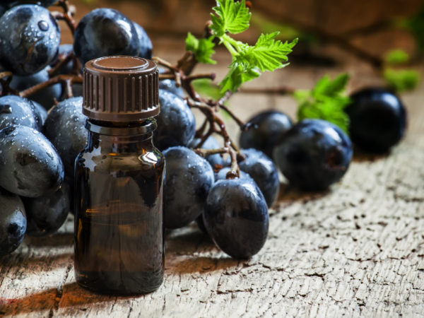 Grape seed oil in brown bottle, bunch of grapes, vine at the old wooden background, selective focus