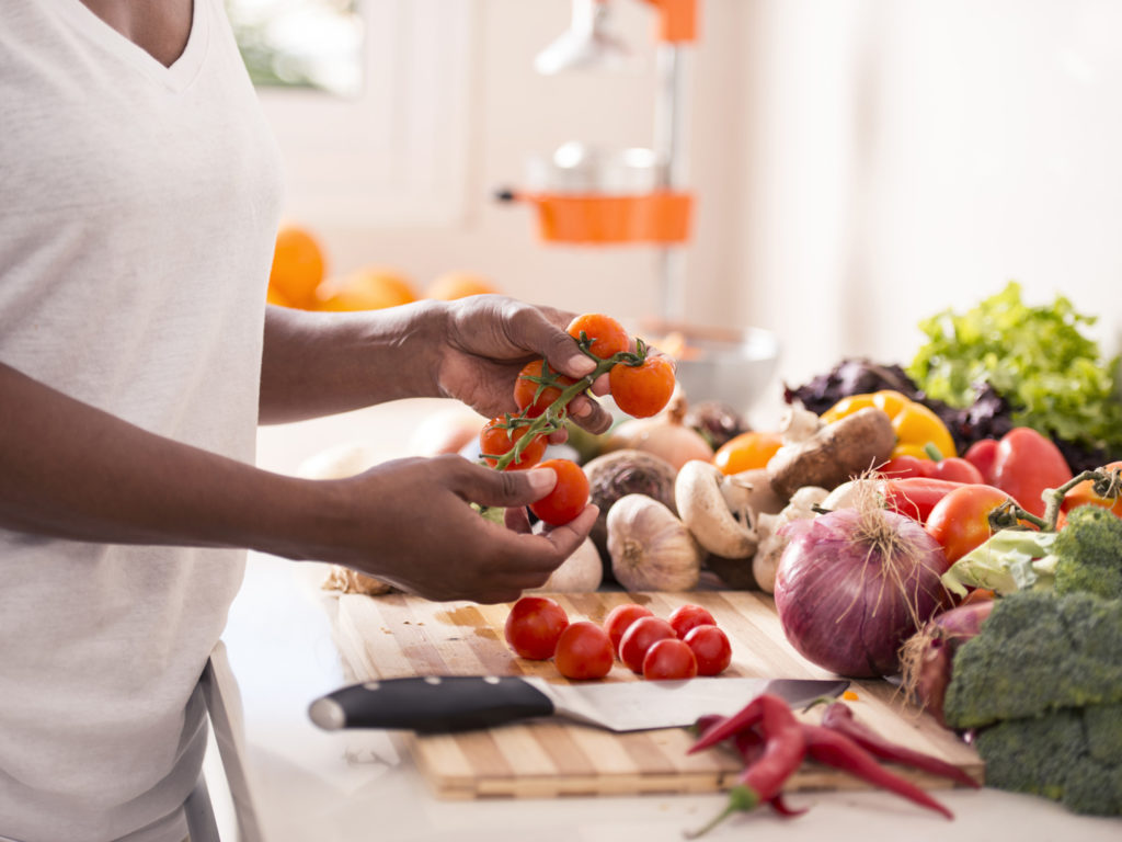 woman preparing salad, holding cherry tomato in hands. Wide variety of vegetables are on background.