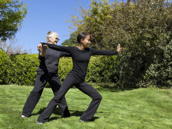 senior woman teaching Tai Chi exercises to young African American woman - outdoors