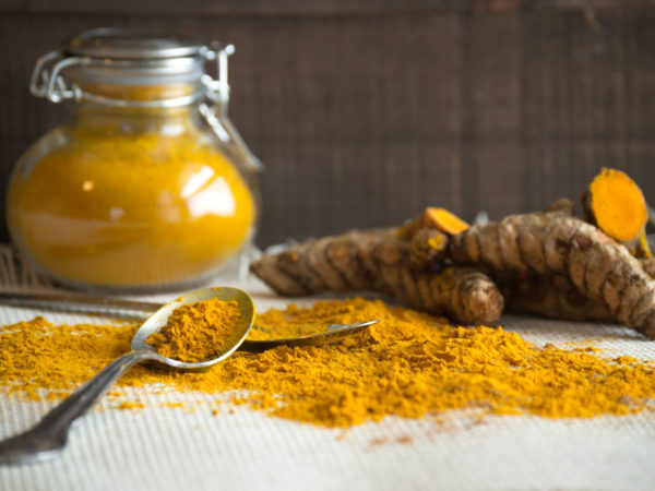 Turmeric root and ground turmeric may help with anti-aging. Add to food, use as a tonic, or display a healthy lifestyle. Black background, classic spice jars displayed raw with root, spice and spoons