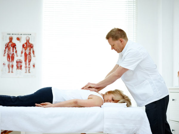 Male osteopath treating back problem of a woman lying on medical room