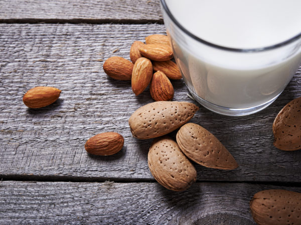glass of almond milk and almond seeds on wooden background