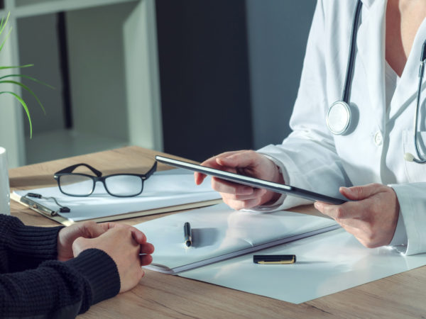 Female doctor presenting medical exam results to patient using digital tablet computer in hospital office