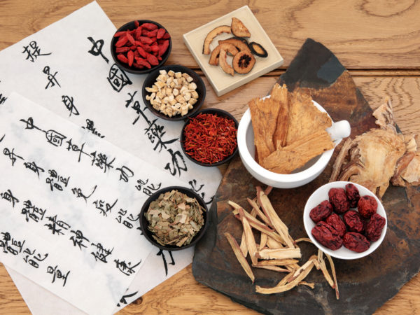Traditional chinese herbal medicine selection with mandarin calligraphy on rice paper over oak. Translation describes the medicinal functions to increase the bodys ability to maintain body and spirit health and balance energy.