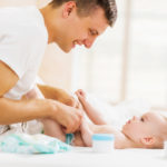 Young father changing diapers to his baby boy in bedroom.