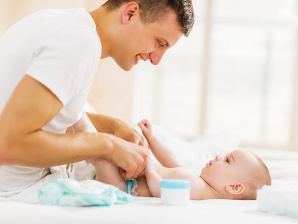 Young father changing diapers to his baby boy in bedroom.