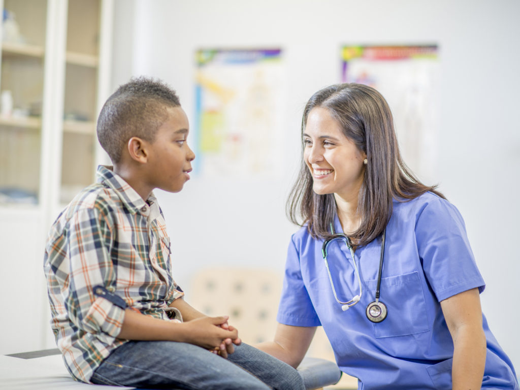 A nurse is talking to the patient who is sitting on the examination table.