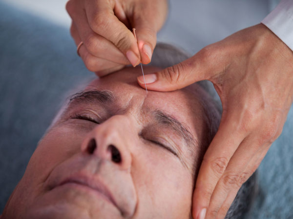 Senior man receiving head massage from physiotherapist in clinic